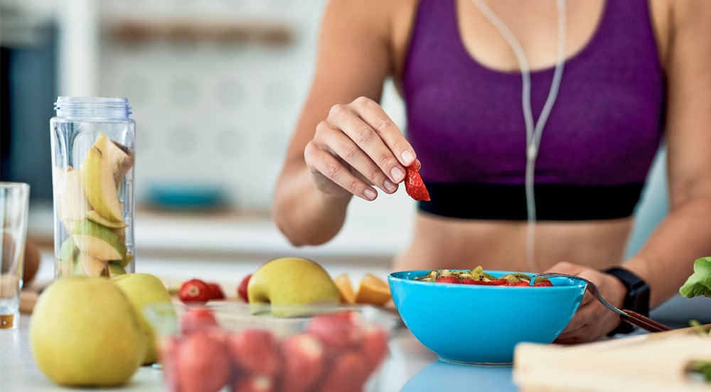 Lybe Clinic: mulher atrás de mesa com frutas para seguir sua nutrição esportiva